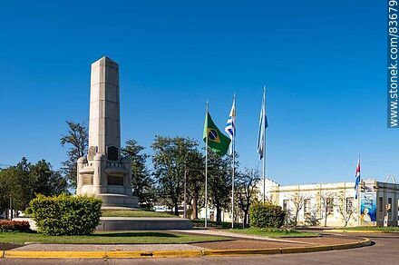 Obelisco y banderas locales e internacionales en la plaza Batlle y Ordóñez - Departamento de Artigas - URUGUAY. Foto No. 83679