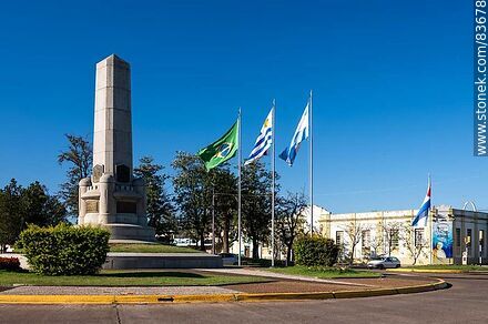 Obelisco y banderas locales e internacionales en la plaza Batlle y Ordóñez - Departamento de Artigas - URUGUAY. Foto No. 83678