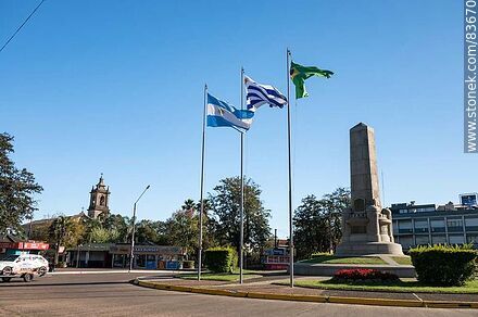 Obelisco y banderas locales e internacionales en la plaza Batlle y Ordóñez - Departamento de Artigas - URUGUAY. Foto No. 83670