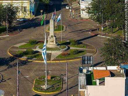 Aerial view of the obelisk and traffic circle at Batlle y Ordóñez square and its flags. - Artigas - URUGUAY. Photo #83639