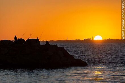 Silueta de pescadores con el sol desapareciendo por debajo del horizonte. A lo lejos el ex frigorífico Swift en el Cerro - Departamento de Montevideo - URUGUAY. Foto No. 79057