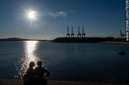 Silhouette of a couple sitting on the Sarandí breakwater in contrast with the reflection of the sun on the river - Department of Montevideo - URUGUAY. Photo #79206