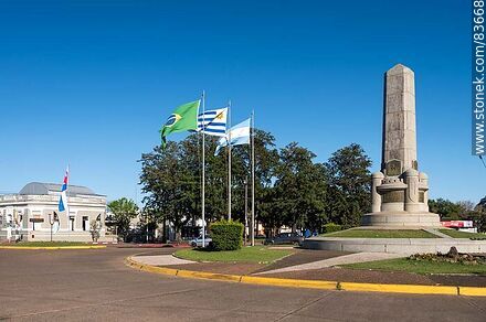 Obelisco y banderas locales e internacionales en la plaza Batlle y Ordóñez - Departamento de Artigas - URUGUAY. Foto No. 83668